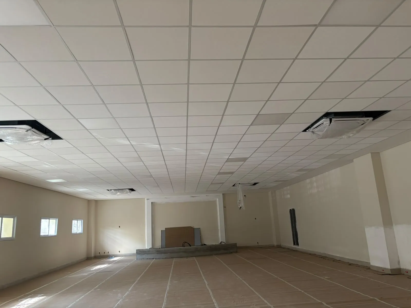 Salão amplo com forro modular instalado e piso protegido durante a obra